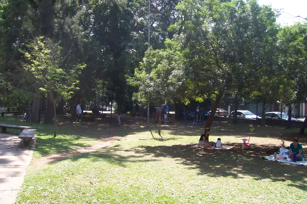 Gramado sombreado por árvores altas no Parque Severo Gomes, com famílias sentadas em toalhas de piquenique