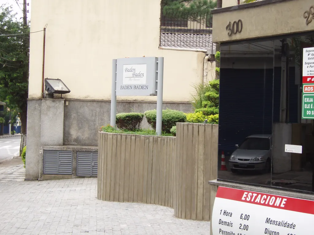 Calçada da Rua Vieira de Morais em frente a um edifício residencial, com placa, jardineira e portão de garagem