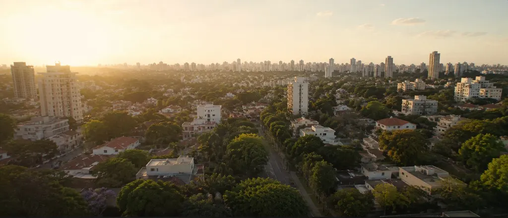 Vista aérea de bairro arborizado ao entardecer, com casas e prédios entre as copas das árvores